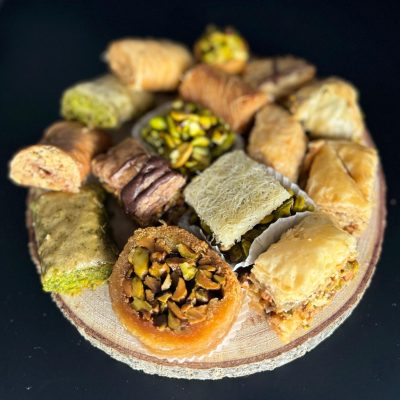 A selection of Middle Eastern pastries arranged on a circular wooden platter, with a dark background.